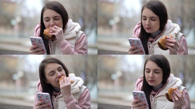 快乐的女人吃汉堡，在街上使用智能手机。