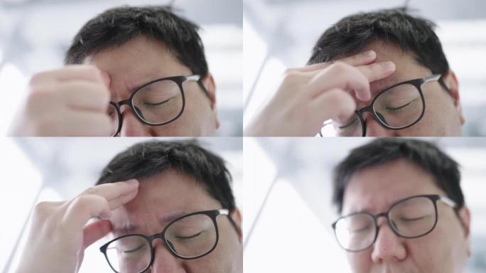 由于严重的头痛，戴着眼镜的年轻人闭上眼睛并用手指在额头上按摩的特写镜头。男人感到不适。
