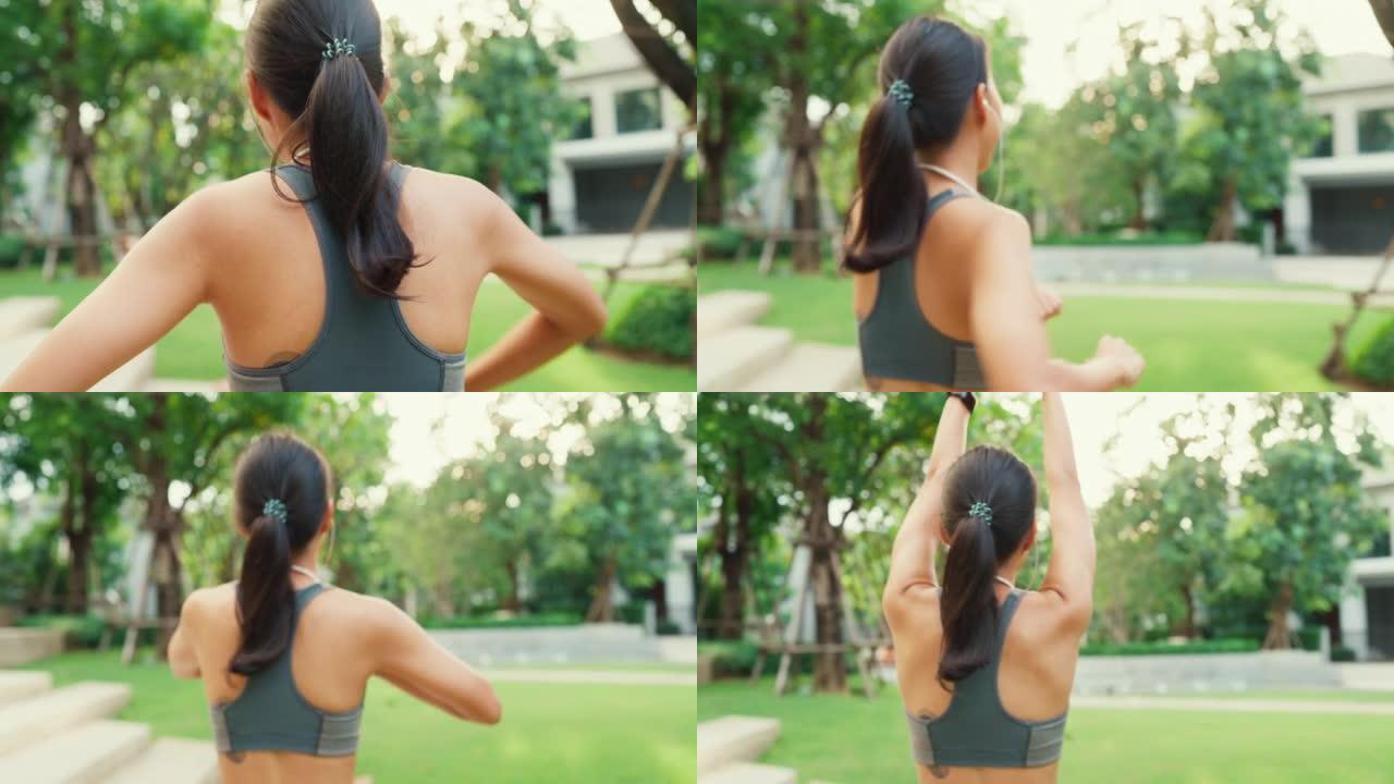 特写快乐的年轻运动型亚洲女性穿着带耳机的运动服，从后角度听音乐，从后角度散步和伸展放松，在花园公园锻