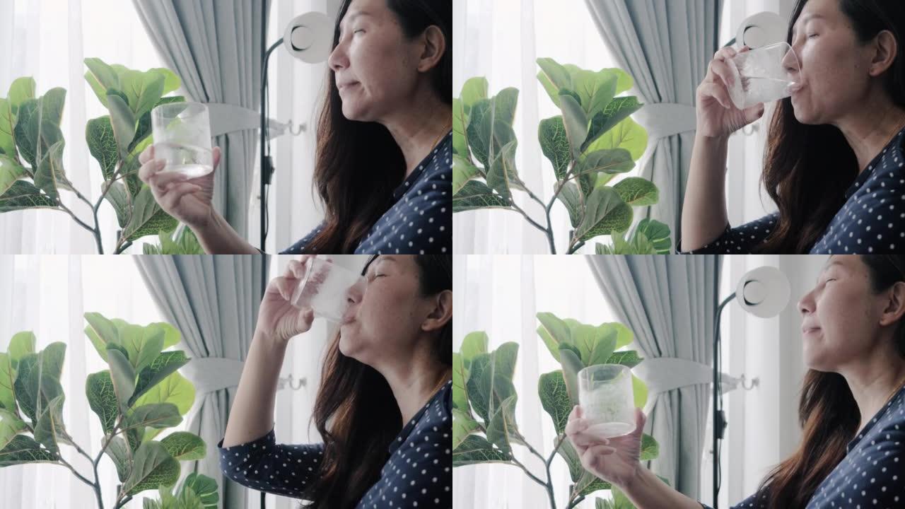 亚洲成年妇女在家中窗户附近喝一杯凉水，简单的生活方式概念。