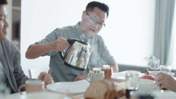 亚洲中国男性在周末为在公寓厨房享用早餐的朋友倒热水煮咖啡