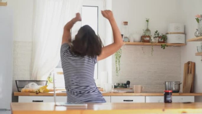 一名年轻的孕妇背对着镜头跳舞。在他家的厨房里欢欣鼓舞。那个女人发现了好消息，玩得很开心。高质量4k镜