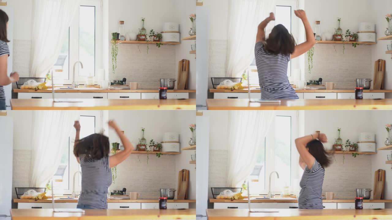 一名年轻的孕妇背对着镜头跳舞。在他家的厨房里欢欣鼓舞。那个女人发现了好消息，玩得很开心。高质量4k镜