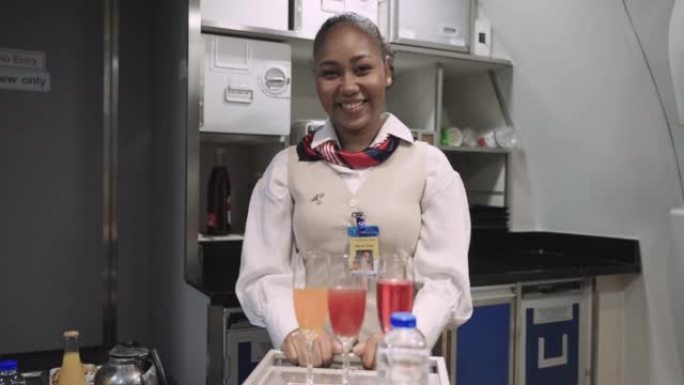穿着制服站在飞机上看着厨房里的相机的快乐非洲女空姐的肖像。