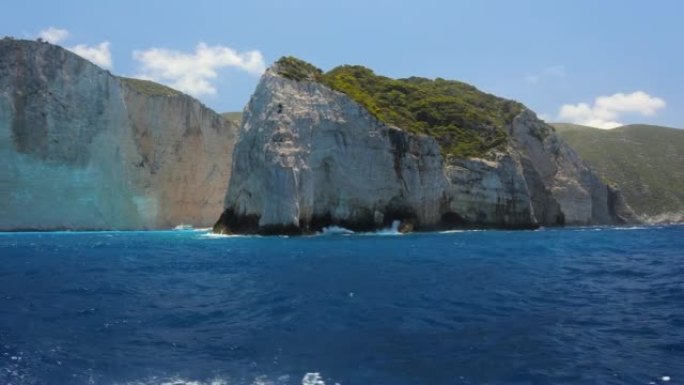 从船上拍摄的蓝色平静海中绿色岩石的半圆视图。