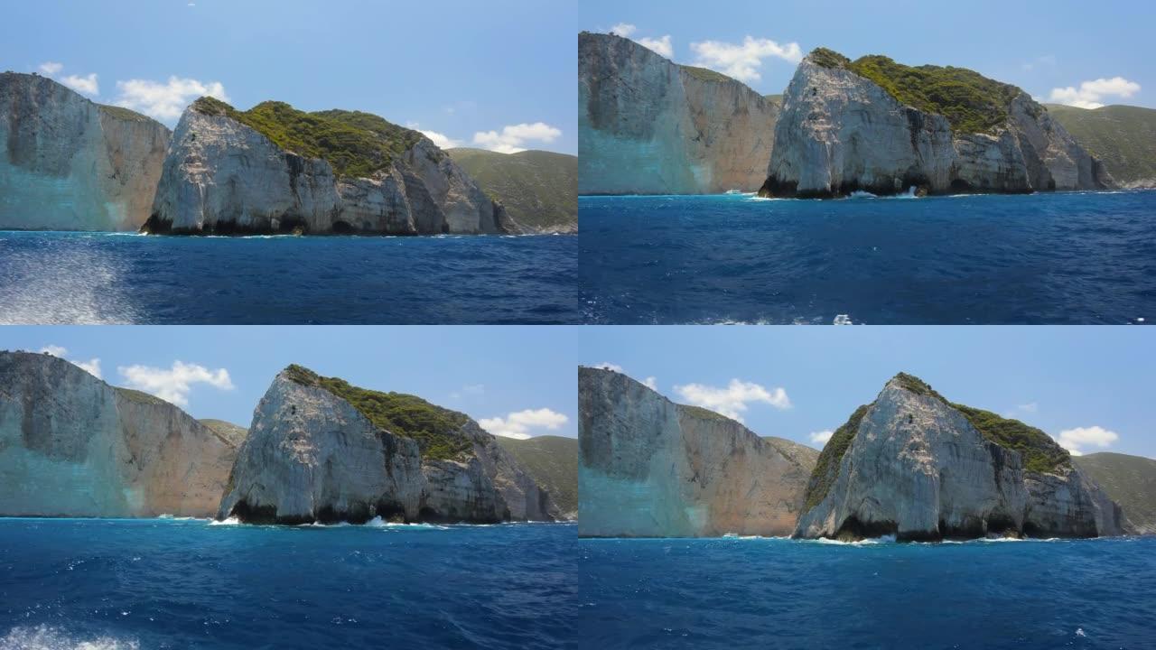 从船上拍摄的蓝色平静海中绿色岩石的半圆视图。