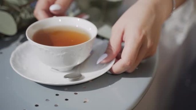 新鲜空气中的白色茶杯站在桌子上。女性手拿一双茶