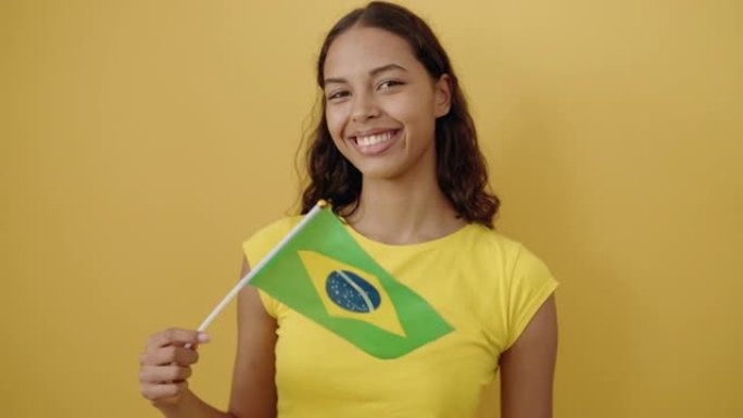 年轻的非洲裔美国妇女微笑着自信地举起巴西国旗在孤立的黄色背景上
