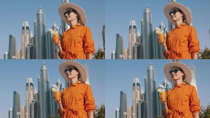 迪拜旅游。城市天际线背景上穿着橙色连衣裙和太阳帽搭配冰沙鸡尾酒的旅游女性。阿联酋的假期