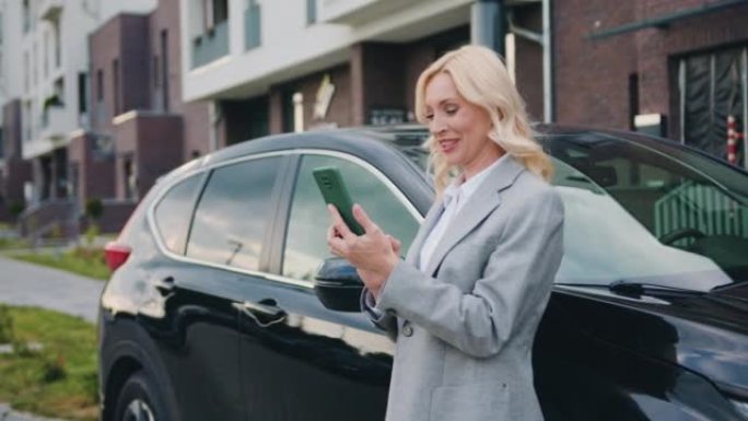 穿着夹克的美丽女商人站在汽车旁，打视频电话。与业务合作伙伴举行会议，讨论新的业务构想