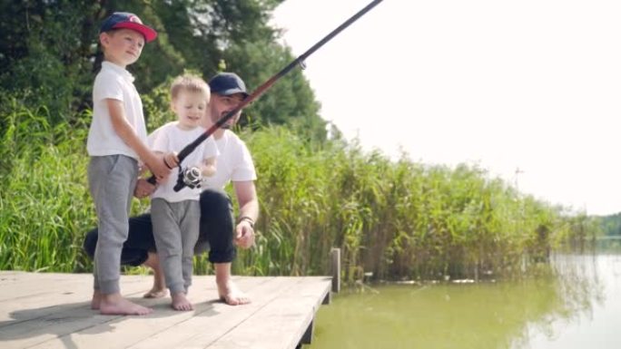 父亲带着小孩儿子站在木桥或码头上抓鱼。家庭爸爸和孩子们一起度过休闲时光露营教钓鱼