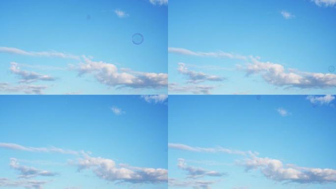 肥皂泡在蓝天下慢慢飞舞。白云笼罩着天空下的漂浮气泡。童年，阳光明媚的温暖日子的户外活动和游戏