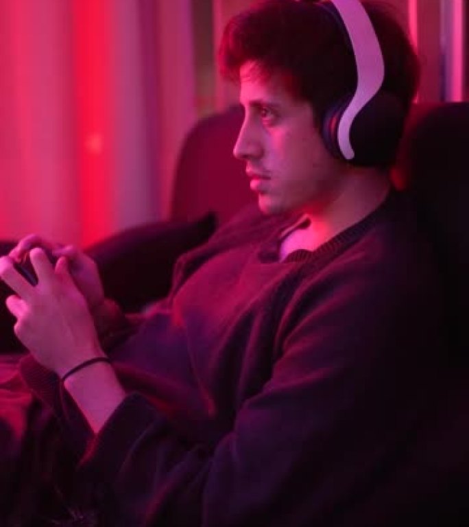一个专心玩电子游戏的人戴着耳机微笑着看着电视屏幕的灯光更加电影化 (垂直)