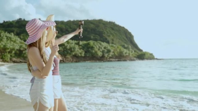 两名亚洲女性博客作者正在与action cam合影，在海上小岛上的海滩旅行中向社交媒体上的朋友炫耀，