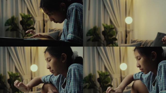 穿着睡衣的亚洲女孩在晚上在家的沙发上通过移动应用学习弹奏键盘乐器，生活方式概念。