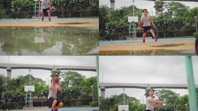 慢动作平移镜头。亚洲男子在日落时在户外球场上玩得开心，弹跳球和运球。男子篮球运动员在野外练习篮球。运