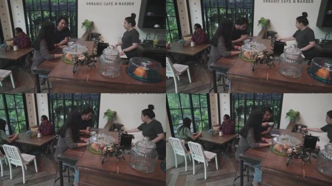 东南亚夫妇围坐在餐桌旁，在咖啡馆里聊天，与咖啡店老板点饮料
