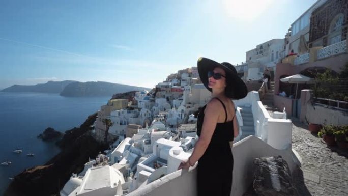 在希腊圣托里尼岛，快乐的女人穿着优雅的黑色衣服和帽子享受假期