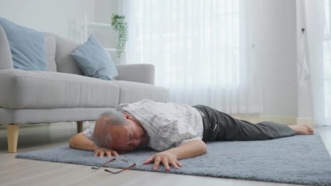 亚洲老年男性在房子里独自行走时摔倒在地上。成熟的老爷爷在家里的客厅退休后做物理治疗后出了事故晕倒。