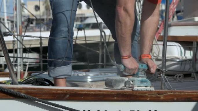 在帆船的栏杆上使用电动砂光机的人。