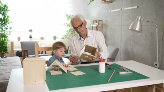 高加索蹒跚学步的男孩帮助他的祖父制作木制鸟舍