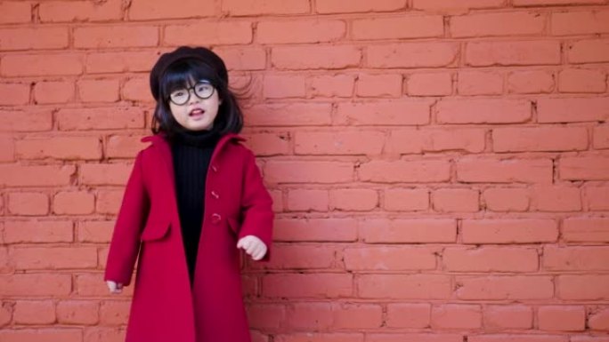 穿着红色外套，帽子和圆形眼镜的韩国女孩在秋天的红砖墙上跳舞