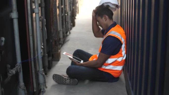 疲惫的工人在进出口货运船的仓库物流的集装箱箱之间用数字平板电脑休息一下