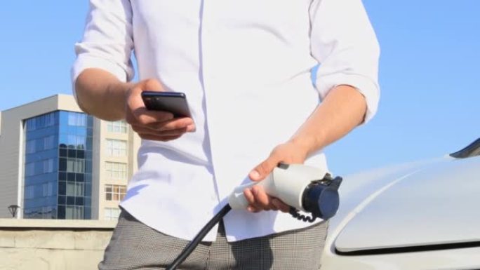 一名成年男子使用智能手机应用程序从一个小型公共车站为汽车电池充电