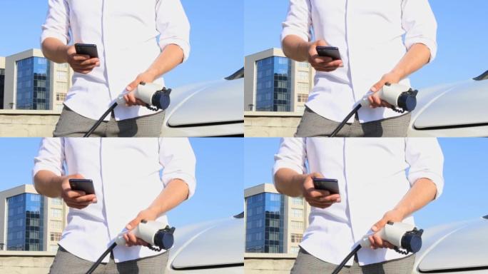 一名成年男子使用智能手机应用程序从一个小型公共车站为汽车电池充电