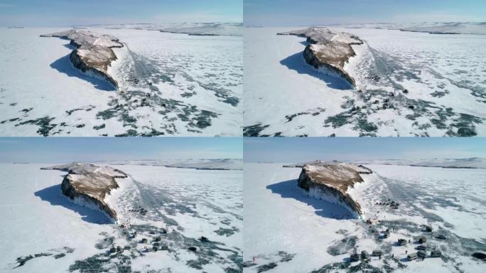 贝加尔湖岩石冰覆盖的岛屿上的鸟瞰图。成群的游客在裂开的冰上走来走去。汽车在冰上行驶。著名的旅游景点。