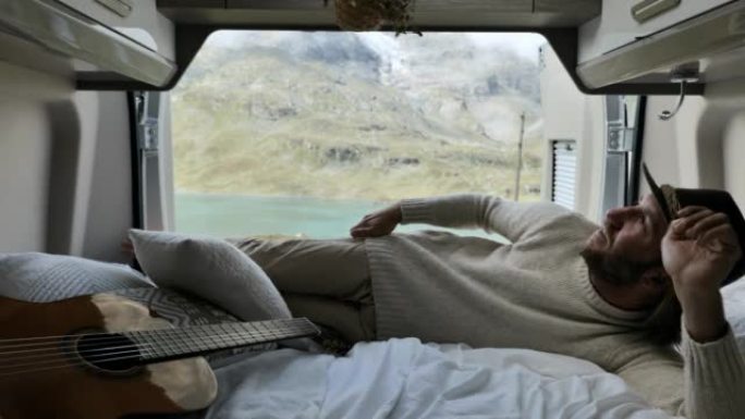 一名男子在一辆可以俯瞰高山湖泊的面包车后面休息