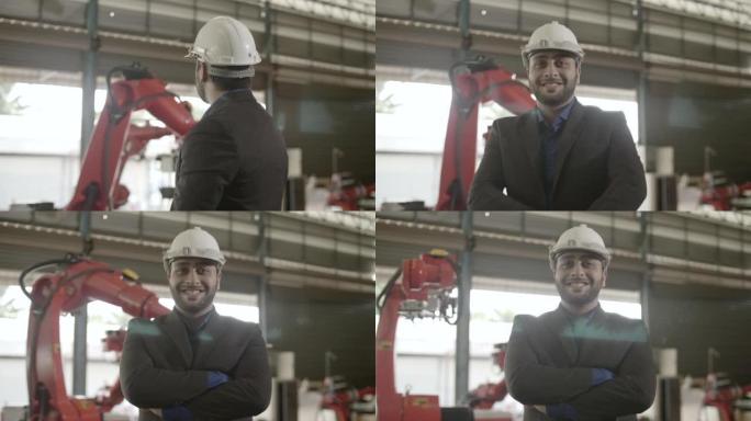 中年工程师在工厂内戴着安全帽看着相机，机器人手臂在背景中移动