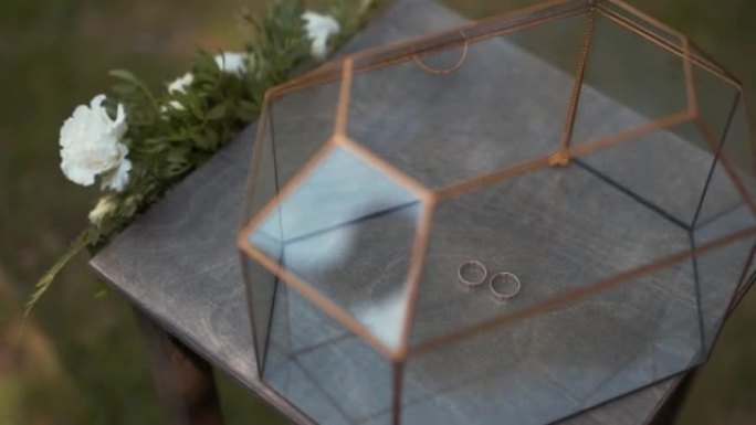 透明玻璃盒中的结婚戒指，棺材站在木桌上
