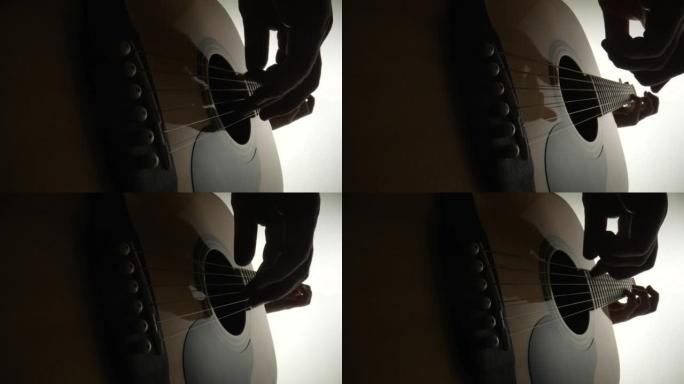 男性吉他手在白色背景上弹奏木制原声吉他的低角度视图。音乐家的手触摸琴弦。吉他的琴弦振动以再现歌曲的音