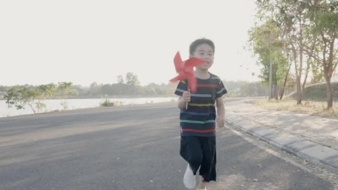 亚洲童子跑着玩着风车，幸福的小男孩拿着小风轮在麦田里微笑