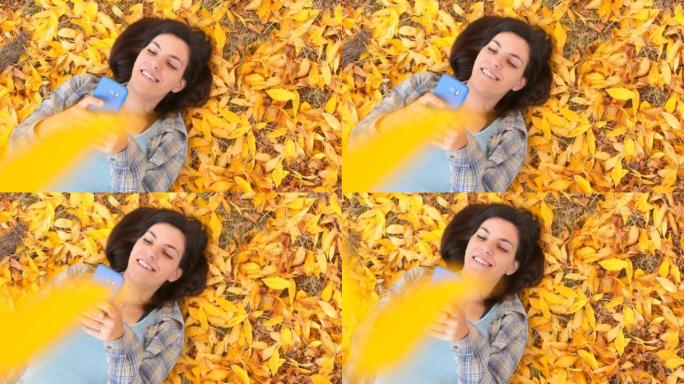 Young Woman Lying On Autumn Leaves And Using Phone
