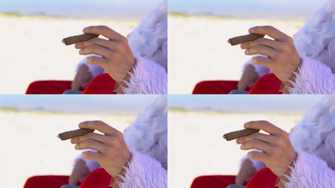 戴着墨镜的圣诞老人躺在沙滩上的日光浴躺椅上抽古巴雪茄。热带地区的圣诞老人