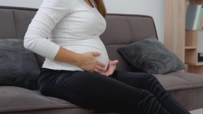 一位皮肤白皙的孕妇坐在舒适的沙发上抚摸着她的肚子