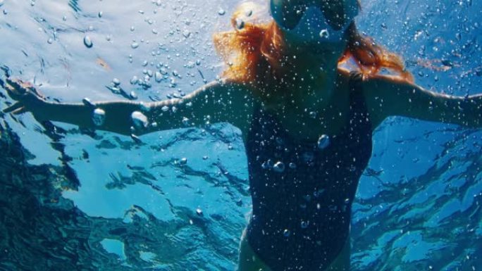 戴着白色面具的女人在马尔代夫的热带海洋中游泳和浮潜，有很多气泡