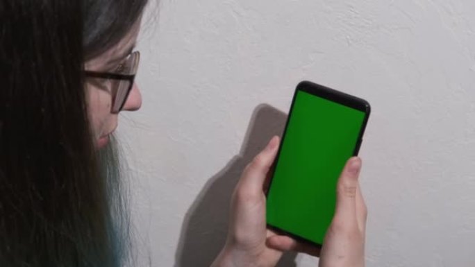 女孩使用智能手机与绿屏色度键。女孩在智能手机屏幕上滑动手指，模仿浏览社交网络，应用程序，购物