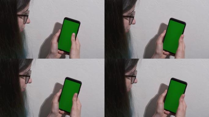 女孩使用智能手机与绿屏色度键。女孩在智能手机屏幕上滑动手指，模仿浏览社交网络，应用程序，购物