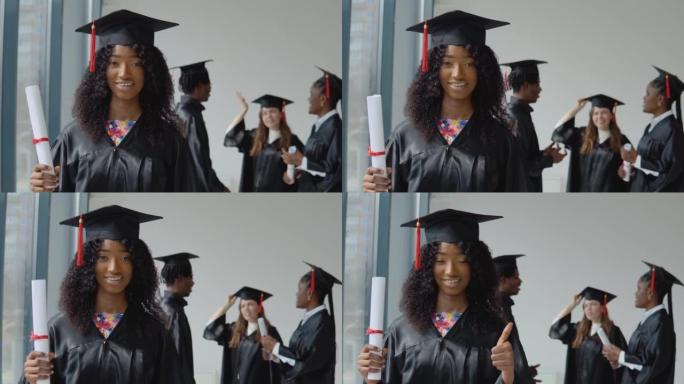 一位年轻的非裔美国妇女站在前台，手里拿着文凭看着相机。年轻的非洲裔美国男女和一名白人妇女在背后交流。