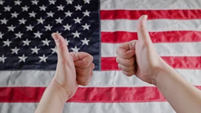 两个白人的手在模糊的美国国旗前做着大拇指朝上和大拇指朝下的手势