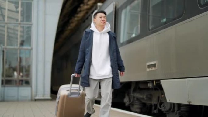 男子亚洲乘客乘火车到达或离开镇上的家，带着大手提箱，铁路火车站的游客男性旅行者在站台上