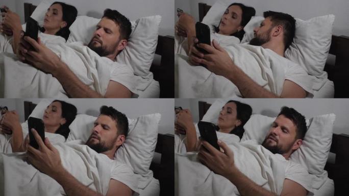 白人夫妇躺在床上睡觉前使用智能手机的特写镜头。男人和女人观看视频并浏览社交网络的提要