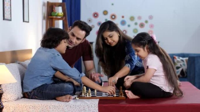 一对迷人的印度夫妇和他们的儿子和女儿在玩棋盘游戏-下棋，一种智能游戏