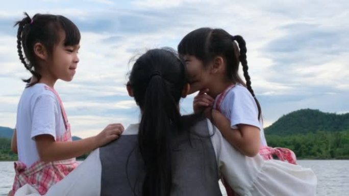 快乐的母亲拥抱着可爱的小姐妹，享受着湖边的大自然。幸福的家庭，母亲和女儿在公园里玩耍，感觉快乐。
