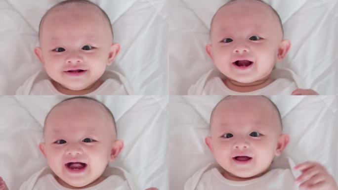脸部特写肖像可爱的亚洲新生婴儿躺在白色床上玩耍看着相机笑着笑脸。天真的小新婴儿可爱。