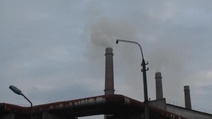 在多云的天空中追踪三个热电联产烟囱的镜头。烟雾冒出来。全球变暖、环境灾难和使用不可持续燃料的概念
