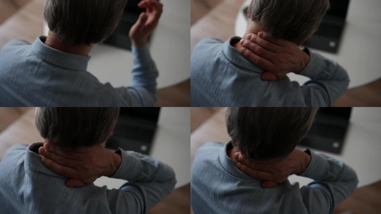 无法辨认的成熟白发男性的特写镜头在笔记本电脑上工作时，颈部会出现剧烈疼痛，摩擦以缓解肌肉紧张。